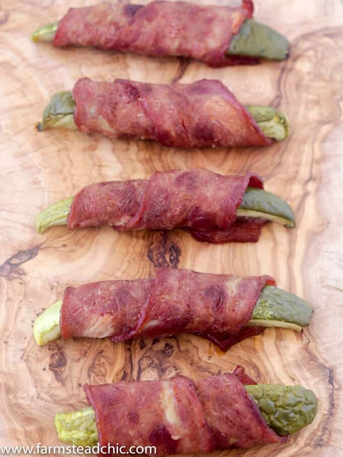 Bacon-wrapped pickles on a natural wood cutting board