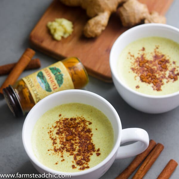 Two Paleo and Whole30 Ginger Turmeric Lattes with cinnamon sticks, fresh ginger and a bottle of ground turmeric.